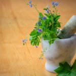 Marble mortar and pestle with fresh herbs and flowers on wooden table enhancing natural health and cooking aesthetics.